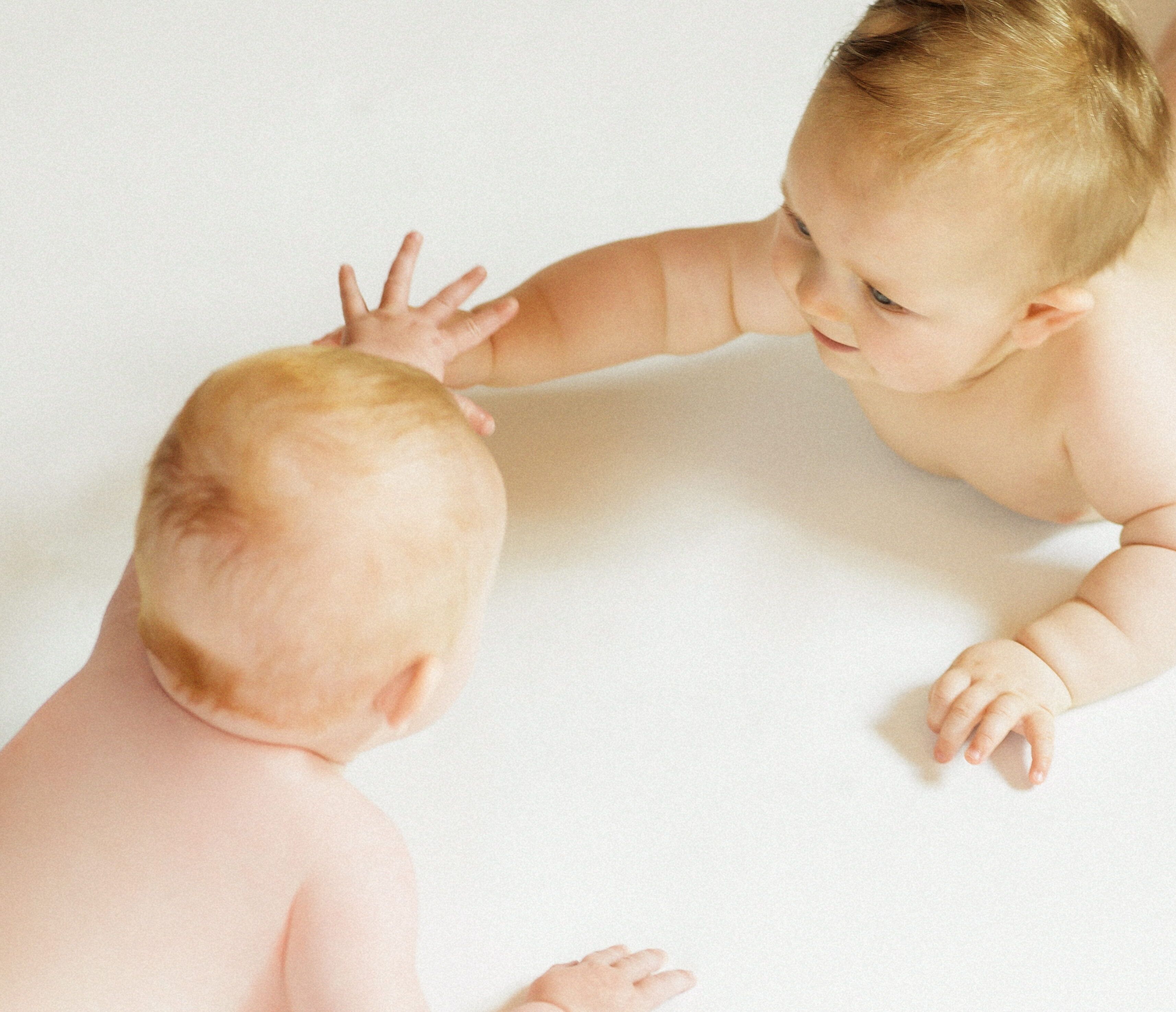 Zwei Babys mit Blickkontakt strecken ihren Hände zueinander